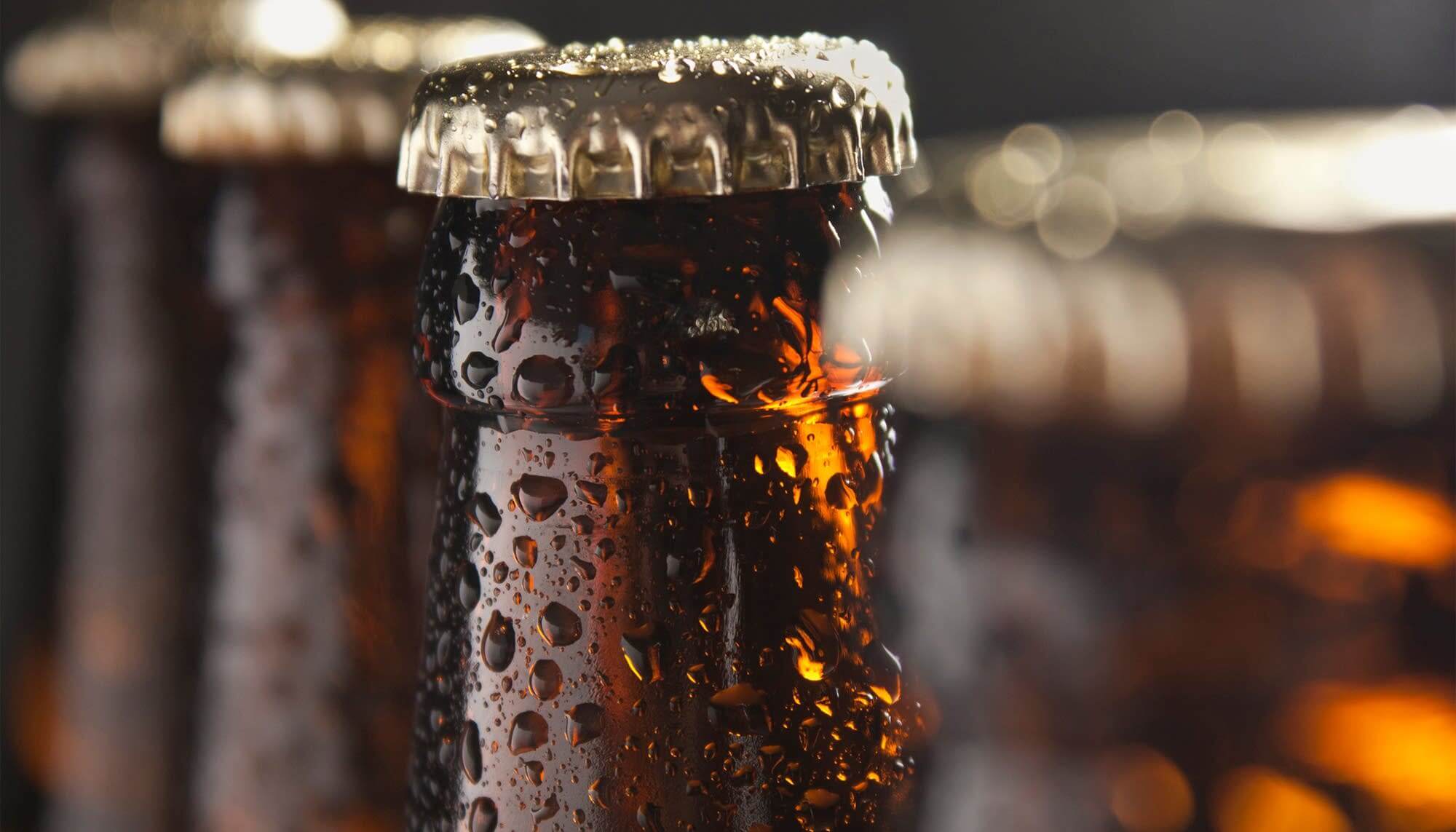 Close-up of a glass beer bottle with condensation and a metal cap, highlighting its refreshing appearance.