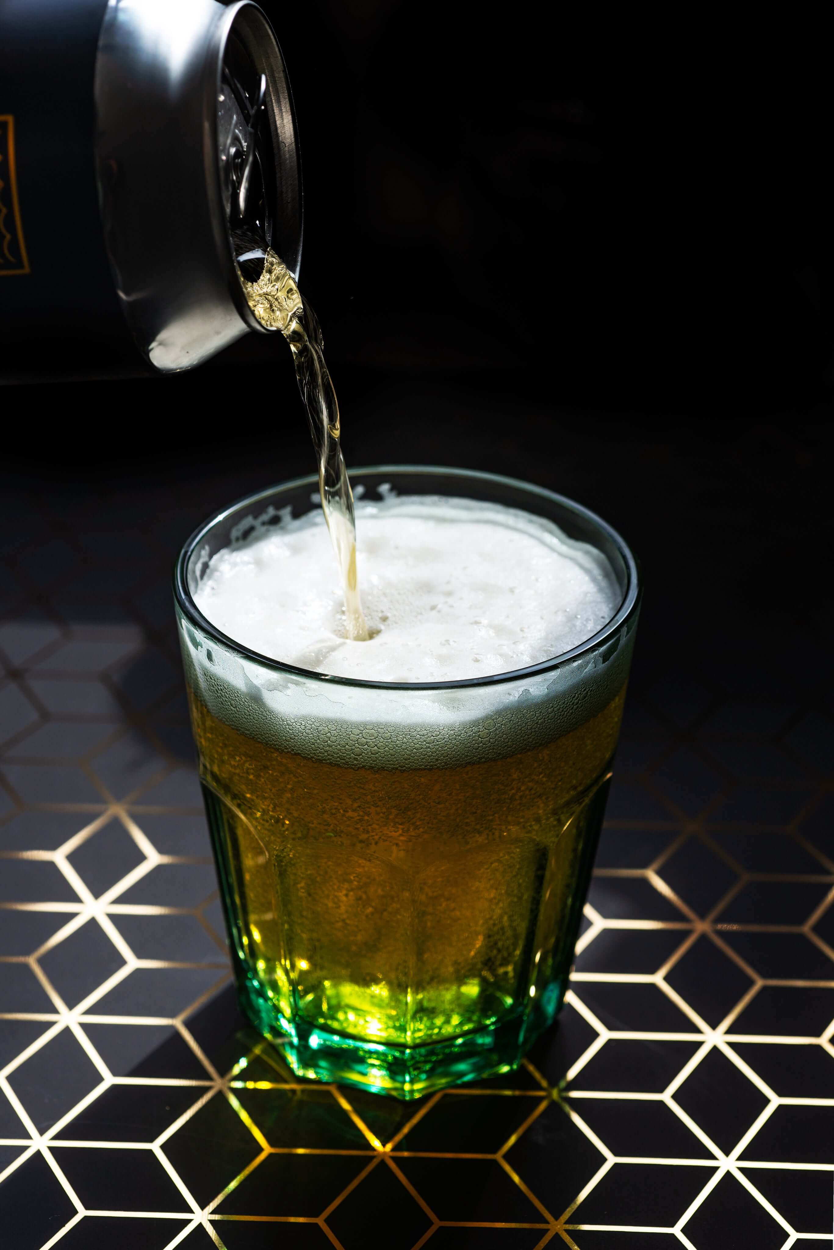 Pouring a golden beer into a frosty glass with foam, set against a stylish geometric background.
