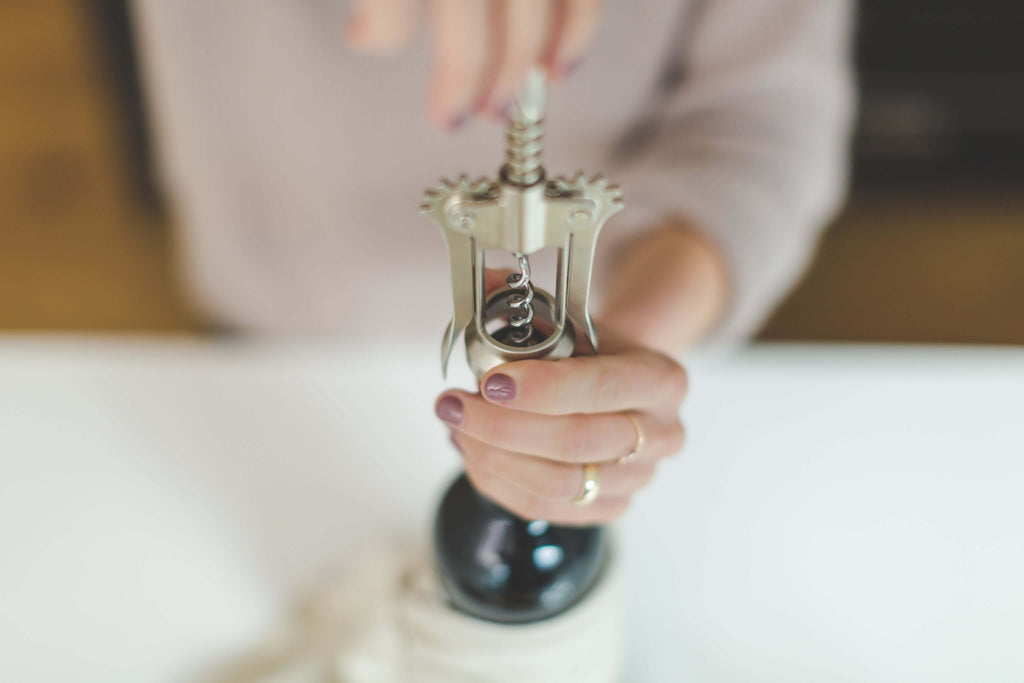 A person using a corkscrew to open a bottle of wine in a cozy kitchen setting.