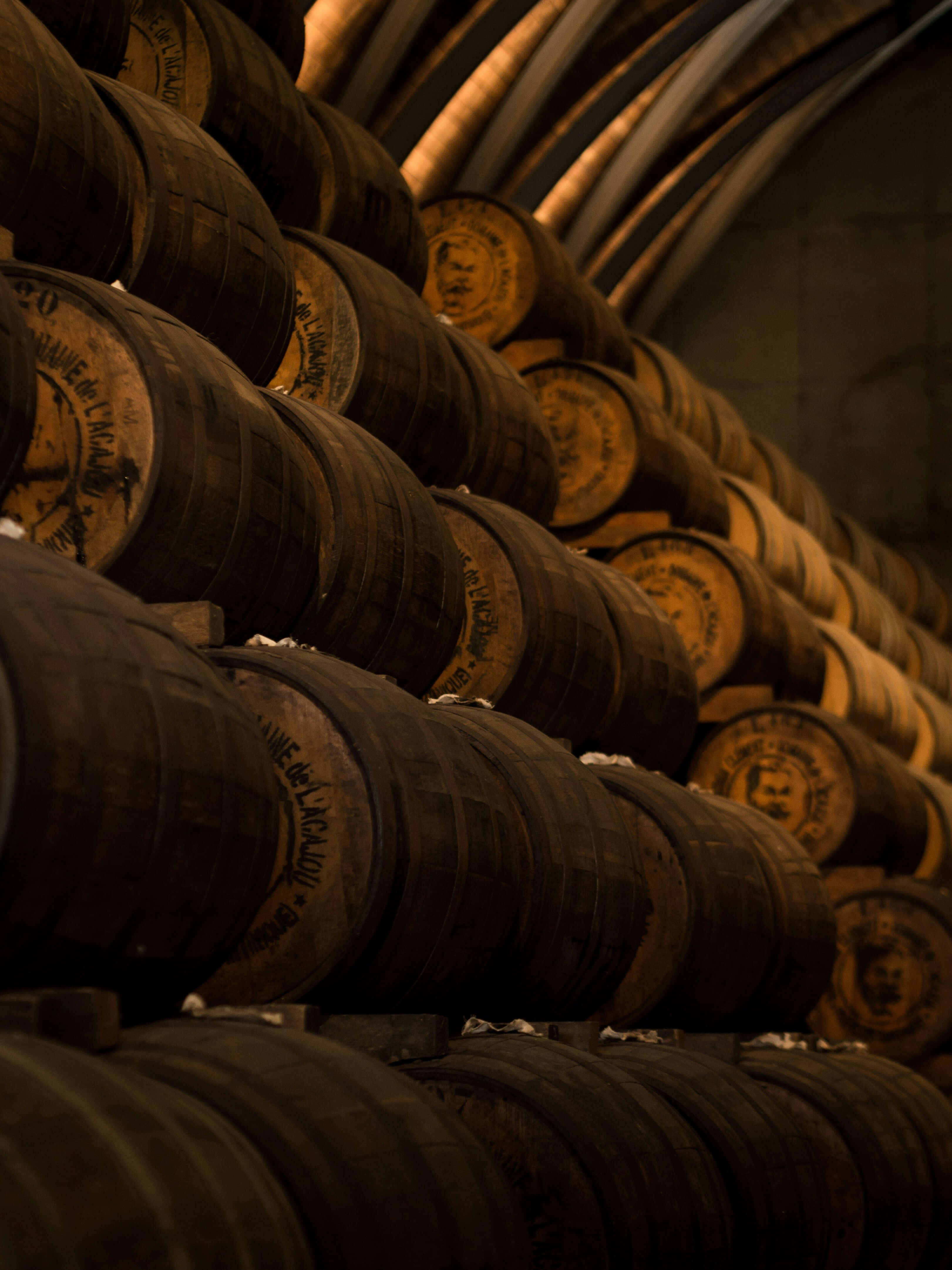 Stacks of wooden barrels in a dimly lit wine cellar, showcasing rich textures and warm tones.