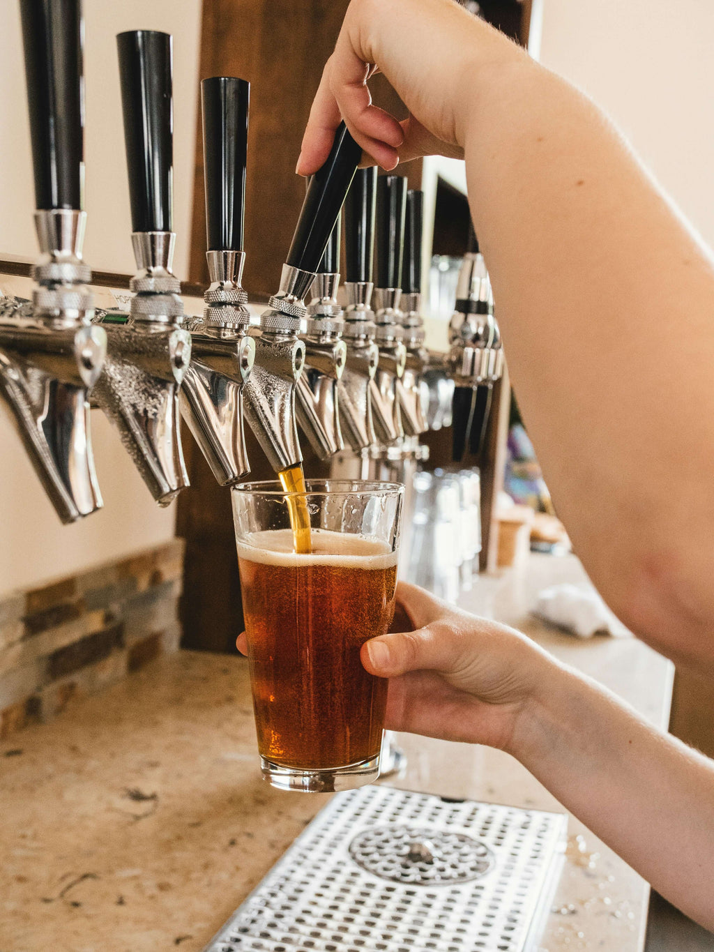 Close-up of a hand pouring a cold beer from a tap into a glass at a bar.
