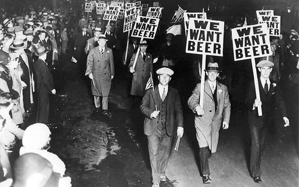 Historical protest march with demonstrators holding signs that read 'We Want Beer' during the Prohibition era.