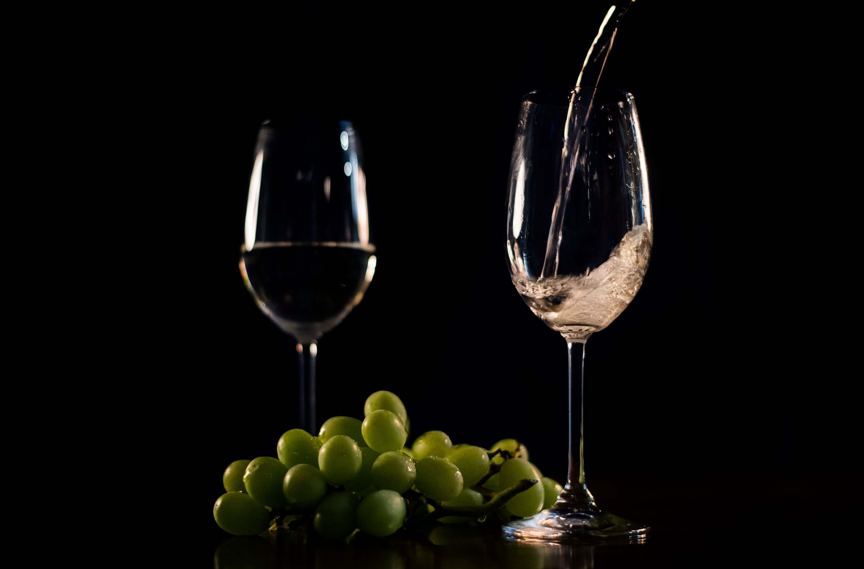 Pouring water into a wine glass next to fresh green grapes, in a dark setting.